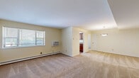 This single-floor residence offers a practical and comfortable layout across two bedrooms, one bathroom, a living room, and a kitchen. The interior is finished with neutral cream-toned walls throughout, creating a consistent and cohesive aesthetic. Carpeting covers the living and bedroom areas, while the kitchen features wood-look flooring for easy maintenance.

The open living area is spacious and well-lit, benefiting from multiple windows with horizontal blinds that allow natural light to filter in. A wall-mounted air conditioning unit and baseboard heating provide year-round climate control. A pendant light fixture marks the transition into the dining area adjacent to the kitchen.

The kitchen is equipped with warm-toned wood cabinetry, granite-style countertops, stainless steel appliances including a dishwasher and gas range, and a full-size refrigerator. In-unit laundry is also accommodated within the kitchen space, adding notable convenience.

The primary bedroom is generously sized, featuring a double closet and direct access to the full bathroom. The second bedroom includes a windowed wall and a single closet. The bathroom is cleanly finished with tile surround, a soaking tub with shower, a vanity with wood cabinetry, and tile flooring.