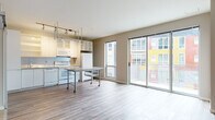 This 1-bedroom, 1-bathroom unit is designed with a clean, modern aesthetic and an open-concept floor plan that seamlessly connects the kitchen and living areas. The kitchen is well-appointed with white cabinetry featuring glass-front upper doors, granite countertops, white appliances including a range, dishwasher, microwave, and refrigerator, and a dedicated overhead track lighting system paired with an industrial-style wire rack for added storage. A movable kitchen island with a granite surface provides flexible workspace and dining options. Large sliding glass doors flood the living area with natural light and open to a private balcony overlooking the vibrant, colorful exterior of the surrounding building. Rich hardwood-style flooring runs throughout the main living spaces, adding warmth and continuity. The bedroom is generously proportioned, featuring exposed utility piping as an industrial design accent, a sliding barn-style door, and access to closet space. The bathroom offers a full tub-shower combo with white tile surround, a granite-topped vanity, geometric-patterned tile flooring, and built-in open shelving for convenient storage. This unit combines contemporary finishes with functional design for comfortable, modern living.