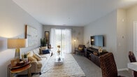This single-floor residence at 1375 S White Oak Dr in Waukegan, Illinois, offers a thoughtfully designed layout with a comfortable and modern aesthetic throughout. The living room serves as the heart of the home, featuring soft carpeting, neutral gray walls, and a large sliding glass door dressed with sheer vertical blinds that flood the space with natural light and provide access to an outdoor area. The open, airy atmosphere is complemented by a wall-mounted flat-screen television and ample room for seating and entertaining. The kitchen is well-equipped and highly functional, showcasing rich dark espresso cabinetry that extends to the ceiling for generous storage, bright white countertops, stainless steel appliances including a range, microwave, and refrigerator, and durable wood-style flooring that adds warmth to the space. The bedroom is a serene retreat, with plush carpeting, neutral tones, and a large window that invites natural light and outdoor views. The full bathroom features a dual-sink vanity with dark cabinetry, a large mirror with overhead lighting, wood-style flooring, and a shower-tub combination, offering both style and practicality. Overall, the space presents a cohesive, contemporary design with consistent finishes throughout.