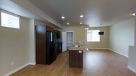 This three-floor space showcases a thoughtfully designed open-concept main living area that seamlessly integrates the kitchen and living room. The kitchen is equipped with dark espresso cabinetry, a suite of black appliances including a French door refrigerator and range, and a granite-topped island with an undermount sink that doubles as a breakfast bar. Recessed lighting illuminates the kitchen area, while a pendant light fixture anchors the dining space nearby. A built-in open shelving unit provides additional storage and display space adjacent to the kitchen. The living area extends naturally from the kitchen, benefiting from natural light through a sizeable window. Light-toned hardwood flooring runs consistently throughout the open-concept space, creating a warm and cohesive aesthetic. The neutral wall tones complement both the dark cabinetry and light flooring, giving the space a balanced, contemporary feel. The layout is notably spacious, offering an easy flow between functional zones. With three floors in total, the property provides generous vertical living space beyond what is visible in the main common areas.