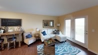 This single-floor 2-bedroom, 1-bathroom residence offers a thoughtfully designed layout that balances comfort and practicality. The living room serves as the heart of the home, featuring warm hardwood-style flooring, soft yellow-toned walls, and a set of full-length French doors that invite abundant natural light and provide outdoor access. The open, airy feel of this space makes it ideal for both relaxing and entertaining.

The kitchen is well-equipped with rich dark espresso cabinetry, granite-style countertops, and black appliances including a range, dishwasher, and over-the-range microwave. The hardwood-style flooring continues here, complementing the cabinetry for a cohesive look.

Both bedrooms are carpeted and generously sized, each featuring warm neutral walls. The primary bedroom includes a built-in closet with shelving, offering practical storage solutions. The second bedroom, which could also serve as a home office, features a window with outdoor views and neutral carpet flooring.

The full bathroom is finished with a dark vanity, granite-style countertop, a large mirror, hardwood-style flooring, and a shower-tub combination, maintaining the consistent design aesthetic found throughout the residence.