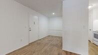 This single-floor unit offers a straightforward, well-maintained layout designed for comfortable everyday living. Consistent light wood-look flooring runs throughout the space, creating a cohesive and easy-to-maintain interior. Crisp white walls and textured ceilings are found across multiple rooms, contributing to a bright, clean aesthetic.

The entryway opens into a welcoming foyer with recessed lighting and a secure entry door equipped with a keypad, providing a functional transition into the living areas. The main living area is generously proportioned, featuring a sliding glass door fitted with vertical blinds that allows natural light to filter in while offering access to the outdoors.

The kitchen is efficiently arranged in a galley-style configuration, outfitted with white cabinetry, light stone-look countertops, a full suite of white appliances including a refrigerator, electric range with overhead ventilation, and a dishwasher. An additional room with a large grid-style window draws in natural light and offers a quiet, versatile space.

A dedicated walk-in closet provides substantial built-in shelving and hanging storage. The full bathroom features a tub-shower combo with white tile surround, a white vanity with countertop, and matching flooring consistent with the rest of the unit.