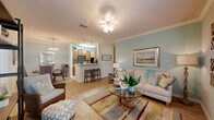 Located at 9905 Windsor Club Dr in Riverview, FL, this two-bedroom, two-bathroom single-floor residence offers a well-designed layout with thoughtful details throughout. Crown molding and light wood-style flooring carry through the main living areas, lending a cohesive and polished feel. The open-concept living, dining, and kitchen area forms the heart of the home, where a bright living room flows seamlessly into a dedicated dining space illuminated by a stylish chandelier. The galley-style kitchen is efficiently arranged with warm wood cabinetry, tile flooring, a full suite of appliances including a range, microwave, dishwasher, and refrigerator, plus a breakfast bar with seating. A welcoming entry hallway connects the living areas to the private quarters, which include two bedrooms each finished with plush carpet and ceiling fans. The spacious primary bedroom features large windows with natural light and ample closet space. Both bathrooms are clean and functional, with one featuring a full tub-shower combination. A dedicated in-unit laundry room with full-size washer and dryer adds everyday convenience. The overall ambiance is light, airy, and well-appointed throughout.