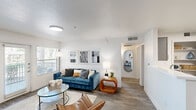 This well-designed single-floor unit offers a thoughtful layout that maximizes its compact footprint. The open-concept living room features wood-style plank flooring, neutral white walls, and natural light from windows fitted with blinds. The space flows seamlessly into the kitchen, which is equipped with stainless steel appliances—including a range, microwave, and refrigerator—complemented by gray cabinetry, white countertops, and an open shelving nook for additional storage. A dedicated in-unit laundry area with a full-size washer and dryer is conveniently positioned adjacent to the kitchen.

The bedroom accommodates a full-size bed and includes a ceiling fan, natural light from a window, and access to a walk-in closet outfitted with multiple hanging rods and open shelving. Three bathrooms serve the unit, with at least one featuring a vanity with gray cabinetry, a white countertop, a lighted mirror with built-in shelving, and a tub-shower combination. The hallway connects all rooms efficiently, contributing to a clean and functional flow throughout the unit.