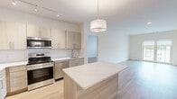 Located at 4180 Sunrise Hwy in Oakdale, NY, this well-appointed 2-bedroom, 2-bathroom residence offers a thoughtfully designed layout spread across a single living floor. The open-concept kitchen and living area serves as the heart of the home, featuring light wood cabinetry, white quartz countertops, a subway tile backsplash, and a full suite of stainless steel appliances including a refrigerator, range, microwave, and dishwasher. A central kitchen island with pendant lighting adds both functionality and style, flowing seamlessly into a bright, expansive living area with light hardwood flooring and natural light from large windows and a glass door leading to an outdoor balcony with views of the community's landscaped grounds and pool area. The generously sized primary bedroom includes dedicated closet space and connects to a private bathroom. The second bedroom is equally well-proportioned, also featuring hardwood floors and dual closet access. Both bathrooms are clean and modern, with wood-toned vanities, light tile flooring, and chrome fixtures. Throughout the residence, a neutral color palette and consistent hardwood flooring create a cohesive, contemporary aesthetic. The community exterior showcases manicured green lawns, a pool, and outdoor lounge seating.