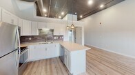 Located at 94 E 11th St in Sioux Falls, South Dakota, this thoughtfully designed single-floor unit blends modern aesthetics with industrial character. The open-concept kitchen serves as the heart of the space, featuring white shaker cabinetry, a subway tile backsplash, quartz countertops, stainless steel appliances, and a central island with pendant lighting overhead. Exposed ductwork and a dark reflective ceiling tile add an urban, loft-inspired feel that contrasts beautifully with the light hardwood flooring below. The adjacent living and dining area benefits from multiple windows that bring in natural light and offer views of the surrounding cityscape. Bedrooms are carpeted for comfort and include generous closet storage with bifold doors and built-in shelving. The primary bathroom is well-appointed with large-format marble-style tile in a glass-enclosed walk-in shower, a dual-sink vanity, and warm neutral tile flooring. A secondary bathroom features a clean, minimalist design with a white vanity, quartz countertop, and brushed nickel fixtures. Throughout the unit, crisp white walls, consistent trim work, and quality finishes create a cohesive and contemporary living environment.
