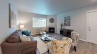 Located at 14615 NE Rose Pkwy in Portland, Oregon, this well-appointed single-floor residence offers a thoughtfully designed layout that balances comfort and functionality. The open-concept living area is a welcoming focal point, featuring warm hardwood-style flooring, neutral tones, and a tile-surround fireplace that anchors the room. Large windows invite an abundance of natural light, creating a bright and airy atmosphere throughout.

The kitchen is a standout space, outfitted with bold dark cabinetry, light quartz-style countertops, stainless steel appliances—including a gas range and refrigerator—and a central island with seating. Sliding glass doors lead to a private outdoor balcony, seamlessly blending indoor and outdoor living. Adjacent to the kitchen, a cozy dining nook provides an intimate setting for everyday meals or entertaining.

Two well-proportioned bedrooms offer restful retreats, each with plush carpeting, natural light from window-fitted walls, and individual climate control units. The bathroom is clean and modern, featuring a glass-enclosed walk-in shower with contemporary fixtures.

Throughout the residence, a cohesive neutral palette and consistent flooring tie the spaces together, resulting in a polished, move-in-ready home in a convenient Portland location.