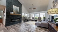 This single-floor community clubhouse is designed with a contemporary aesthetic that balances comfort and functionality throughout. The welcoming entrance foyer sets an immediate tone with soaring vaulted ceilings, wood-look tile flooring, and bold artwork that creates an inviting first impression.

The main lounge area is a standout feature, anchored by a dramatic floor-to-ceiling dark stacked-stone fireplace with a wooden mantle. Vaulted ceilings, a modern ceiling fan, and an expansive array of large windows flood the space with natural light and provide open views of the surrounding greenery. The seating area includes a tufted sectional sofa, classic wingback chairs, and a vibrant geometric area rug that adds warmth and color.

Adjacent to the lounge is a reception and business area, featuring a service counter, workspace with computer access, and continued wood-look tile flooring. A casual high-top bar table with industrial-style stools offers a relaxed workspace near the windows.

The fitness center is generously sized, with high vaulted ceilings and ceiling fans providing ventilation. It is well-equipped with cardio machines including treadmills and ellipticals, a full dumbbell rack, a weight bench, a punching bag, and a cable machine. Rubber flooring and large windows with outdoor views complete the energizing environment throughout the space.