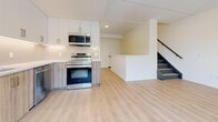 Located at 97 Milford Ave in Waterloo, Ontario, this modern two-storey unit offers a thoughtfully designed layout spread across two floors. The main level features a contemporary open-concept kitchen equipped with stainless steel appliances, including a range, over-the-range microwave, and dishwasher, complemented by crisp white upper cabinetry, wood-toned lower cabinets, and a classic subway tile backsplash. Light vinyl plank flooring flows throughout both levels, lending warmth and continuity to the space. A striking staircase with light stone-tiled treads, dark metal nosings, and a sleek metal handrail connects the two floors. The upper level hosts bright, airy bedrooms with sliding glass doors opening onto a balcony featuring modern glass-panel railings, offering pleasant views of the surrounding tree-lined neighbourhood. Additional highlights include a full bathroom with a soaker tub and large-format tile surround, a second bathroom with a wood-grain vanity and in-unit stacked laundry, and ample closet space. Neutral warm tones, recessed lighting, and an abundance of natural light throughout create a clean, inviting ambiance well-suited to comfortable everyday living.