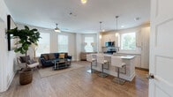 Located at 1630 Peachtree Industrial Blvd in Suwanee, GA, this semi-model 2-bedroom, 2-bathroom residence is designed with a clean, contemporary aesthetic throughout its single-floor layout. The open-concept living and kitchen area serves as the heart of the home, bathed in natural light from multiple windows dressed with white blinds. Wood-look plank flooring flows seamlessly through the main living spaces, complementing the neutral color palette and modern design sensibility.

The kitchen is a functional highlight, featuring light-toned cabinetry, a classic subway tile backsplash, granite countertops, a large island with bar seating, and a full suite of stainless steel appliances including a French door refrigerator. Pendant lighting above the island adds a polished touch. The adjoining living area is generously proportioned, complete with a ceiling fan and ample room for comfortable furnishings.

A hallway connects the bedrooms and bathrooms, maintaining a clean and organized flow. The primary bedroom is a calm retreat with plush carpet, a ceiling fan, and closet space. The secondary bedroom similarly offers natural light and a relaxed ambiance. Both bathrooms feature granite-topped vanities, wood-look flooring, and tub-shower combinations, providing a cohesive and practical finish throughout.