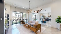 This contemporary clubhouse in Denham Springs, Louisiana, delivers a striking first impression through its grand entry foyer, where soaring vaulted ceilings with exposed wood beam accents and large-format black-framed glass doors set a bold architectural tone. Polished concrete floors flow seamlessly throughout, tying together the open-concept layout with a clean, modern aesthetic.

The expansive main gathering area is bathed in natural light through floor-to-ceiling windows that frame views of the surrounding community. Warm pendant chandeliers and statement lighting fixtures complement the natural wood and woven textures found in the carefully curated furnishings, including rattan accent chairs, live-edge driftwood coffee tables, and plush seating arrangements. A large wall-mounted television and built-in display shelving anchor one end of the lounge, while a high-top bar area runs along the windowed perimeter.

A fully equipped kitchen features gray shaker cabinetry, white quartz countertops, a farmhouse sink, subway tile backsplash, floating wood shelves, and premium stainless appliances. Adjacent dining and lounge zones provide flexible seating options for gatherings of all sizes.

Glass-paneled sliding doors lead to private rooms suited for meetings or events. Curated artwork, including a dramatic landscape triptych, adds a refined, gallery-like quality to the overall ambiance of this well-appointed community amenity space.