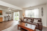 This two-story home offers a thoughtfully designed layout spread across two levels, connected by a central staircase visible in the floor plan. The kitchen is a functional centerpiece, featuring warm oak cabinetry, granite-look countertops, hardwood-style flooring, and stainless steel appliances including a refrigerator, gas range, and dishwasher. A ceiling fan overhead and a casual bar-height dining area complete the space. The living room provides a comfortable gathering area with plush carpet, neutral walls, and natural light from a front-facing window. Two bedrooms are present, each carpeted and well-sized. The primary bedroom benefits from multiple windows that invite generous natural light, a ceiling fan, and ample floor space. The second bedroom is cozy and practical. Two bathrooms serve the home — one full bath with a tub-shower combination, wood-tone vanity, and hardwood-style flooring; and a second bathroom with a similar aesthetic, accented with ocean-themed décor. A dedicated laundry room houses a full-size top-load washer and dryer, adding everyday convenience. Throughout the home, consistent warm-toned finishes, neutral walls, and wood-style flooring in key areas create a cohesive and inviting atmosphere.
