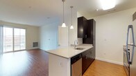 This single-floor, 2-bedroom, 2-bathroom residence offers a thoughtfully designed open-concept layout that maximizes functionality and flow. The kitchen serves as a central focal point, featuring dark espresso cabinetry that contrasts elegantly with light granite countertops. A peninsula island with an undermount sink provides additional prep space and casual seating potential, while stainless steel appliances, including a dishwasher, add a modern, polished touch. Dual pendant lights hang above the peninsula, providing focused task lighting with a contemporary aesthetic.

The kitchen opens seamlessly into the living area, creating a connected and sociable space suited for both everyday living and entertaining. Warm hardwood-style flooring flows throughout the main living areas, adding a cohesive and inviting feel to the space. Neutral white walls provide a versatile backdrop, allowing for a variety of décor styles. The living area benefits from natural light, contributing to an airy and open ambiance. Overall, the residence combines modern design elements with practical features, offering a clean, comfortable, and move-in-ready living environment.