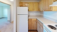 Located at 151 North in Portland, Maine, this single-floor unit offers a practical and comfortable layout designed for everyday living. The open living area is finished with neutral wall-to-wall carpeting and features a baseboard heating system, while a set of French doors fills the space with natural light and provides outdoor access. The kitchen is thoughtfully appointed with light wood cabinetry — including upper and lower storage — laminate countertops, and standard appliances including a full-size refrigerator. A pass-through peninsula connects the kitchen to the living area, creating an open and sociable flow between the two spaces. The unit includes multiple carpeted bedrooms, each featuring baseboard heating and windows that look out onto green outdoor surroundings, allowing ample natural light. Two bathrooms serve the unit; both are finished with tile flooring, light wood vanities, white countertops, and medicine cabinet storage. One bathroom includes a bathtub, while the other is configured as a three-quarter bath. The overall aesthetic is clean, neutral, and functional, making this unit a versatile and move-in-ready space in Portland, Maine.