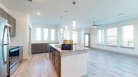 This well-appointed single-floor residence offers a thoughtfully designed open-concept layout that seamlessly connects the kitchen, dining, and living areas. The kitchen is a standout feature, showcasing granite countertops, a large center island with pendant lighting overhead, dark cabinetted lower storage, and stainless steel appliances including a range, microwave, and dishwasher. A classic white subway tile backsplash adds a clean, modern contrast. Light wood-look flooring flows consistently throughout the entire unit, contributing to a cohesive and airy aesthetic. Abundant windows allow natural light to fill every room, while ceiling fans in the main living areas provide both comfort and style. The living space is generously proportioned and opens toward exterior views. Bedrooms are spacious and bright, each with ceiling fans and large windows. The primary bedroom connects directly to a well-sized bathroom featuring a dual-sink granite vanity with bold navy-blue cabinetry, a walk-in shower with glass enclosure, and direct access to a walk-in closet. A dedicated in-unit laundry room with side-by-side washer and dryer adds everyday convenience. The overall ambiance is clean, contemporary, and move-in ready.