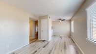 This single-floor unit is constructed with painted concrete block walls throughout, lending a solid, durable character to each room. Light wood-style vinyl plank flooring flows consistently across the living areas and bedrooms, providing a clean, cohesive aesthetic. Textured ceilings and ceiling fans are present in the main living space and bedrooms, contributing to both style and air circulation.

The open living area connects seamlessly to the kitchen via a pass-through counter, creating an efficient, functional layout. The kitchen is equipped with white cabinetry, light quartz-style countertops, a decorative mosaic tile backsplash, and a full-size stainless steel refrigerator, offering a modern contrast to the unit's block construction.

The bedrooms are well-proportioned, each featuring ceiling fans with light fixtures, windows fitted with horizontal blinds for natural light control, and the same durable wood-style flooring found throughout. One room includes direct exterior door access, adding convenience.

The bathroom features warm earth-toned ceramic tile surrounding a soaking tub and shower combination, accented by a decorative mosaic border strip. Wood-style flooring continues into the bathroom, maintaining a unified look. Overall, the space presents a clean, updated interior with practical finishes throughout.