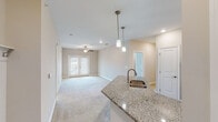 Located at 4650 Crescent Pointe Dr in North Charleston, SC, this single-story home offers a well-designed, open-concept layout that seamlessly connects the kitchen and living areas. The kitchen is a standout feature, equipped with white shaker-style cabinetry, granite countertops, a peninsula with an undermount sink, pendant lighting, and a full suite of stainless steel appliances including a range, microwave, dishwasher, and refrigerator. Warm hardwood-style flooring runs throughout the kitchen and utility areas, adding a cohesive, polished look. The living room is bright and welcoming, featuring plush neutral carpeting, a ceiling fan, recessed lighting, and French doors that invite natural light and provide outdoor access. The bedrooms continue the carpeted flooring and are each equipped with ceiling fans and windows that allow for natural light. Two bathrooms mirror each other in design, each featuring white cabinetry with granite countertops, a tub-shower combination with white subway tile surround, and hardwood-style flooring. A dedicated laundry room accommodates a full-size washer and dryer and includes overhead wire shelving for added storage. The overall aesthetic is clean, neutral, and move-in ready.