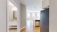 Located at 100 W Water St in Elmira, NY, this well-appointed 2-bedroom, 2-bathroom residence offers a thoughtfully designed single-floor layout with a clean, contemporary aesthetic throughout. The open-concept living and kitchen area serves as the heart of the home, featuring warm hardwood floors, an abundance of natural light from multiple windows, and a seamless flow between spaces. The kitchen is equipped with stainless steel appliances, including a refrigerator, range, and built-in microwave, complemented by crisp white cabinetry, a subway tile backsplash, and an expansive granite-topped island with pendant lighting overhead. Both bedrooms are carpeted and well-lit, offering a comfortable retreat, with the primary bedroom providing a generous footprint and dedicated closet space. The two bathrooms are finished with light-toned tile flooring, white vanities with granite countertops, and glass-enclosed showers. A dedicated entrance, utility room, and two closets add to the unit's practicality. Neutral warm-beige wall tones and white trim carry a cohesive palette throughout, creating a bright and welcoming ambiance suited for everyday living.