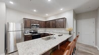 Located at 3861 W University St in Springfield, MO, this two-bedroom, two-bathroom residence offers a well-designed single-floor layout with modern finishes throughout. The open-concept kitchen and living area forms the heart of the home, where rich dark-wood cabinetry, light granite countertops, and stainless steel appliances create a polished, functional kitchen. A large peninsula with an undermount sink and seating provides additional workspace and casual dining. Light hardwood-style flooring flows seamlessly into the spacious living room, which is anchored by a ceiling fan and a sliding glass door that fills the space with natural light and provides outdoor access. The generously sized primary bedroom features plush carpet, a ceiling fan, and a window for natural light, complemented by a walk-in closet with wire shelving and a private en-suite bathroom with granite vanity. The second bedroom is equally well-appointed with carpet flooring, a ceiling fan, and a window. A hallway connects the rooms efficiently, with three closets throughout offering ample storage. The two bathrooms mirror the home's consistent design aesthetic with granite counters and dark cabinetry. Recessed lighting and neutral tones throughout contribute to a clean, contemporary ambiance.