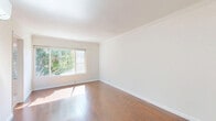 Located in the heart of West Hollywood, this efficiently designed unit on the second floor offers a well-organized layout comprising a living room, kitchen, bathroom, and closet. The living area is the centerpiece of the space, featuring warm-toned hardwood flooring, crisp white walls, and crown molding that adds a clean architectural detail. A large sliding window invites generous natural light and frames a pleasant view of lush greenery outside, creating a bright and airy atmosphere. A wall-mounted mini-split air conditioning unit ensures year-round comfort. The kitchen is outfitted with white cabinetry — both upper and lower — providing ample storage, complemented by a stainless steel refrigerator, a gas range, and light-toned tile flooring that contrasts neatly with the rest of the unit. A utility sink adds practical functionality. The bathroom features a classic white tile surround with a shower-tub combination, maintaining the unit's clean and neutral aesthetic throughout. A dedicated closet offers additional storage. The overall ambiance is light, minimal, and functional — well-suited for those seeking a practical living space in a prime West Hollywood location.