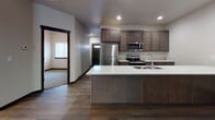 Located at 12007 East Coyote Rock Drive in Spokane Valley, Washington, this single-floor unit offers a well-designed, contemporary layout with a cohesive blend of materials and finishes throughout. The entryway features textured walls and wood-look flooring that flows through the main living areas, creating a warm and consistent aesthetic from the moment you step inside. The open-concept living and dining area is bright and spacious, anchored by a stylish chandelier and complemented by recessed lighting and large vertical blinds that allow for generous natural light. Wood-look plank flooring runs throughout these shared spaces, adding durability and visual warmth. The kitchen is a standout feature, showcasing rich dark-stained cabinetry, a large center island with a white countertop and undermount sink, and a full suite of stainless steel appliances including a refrigerator, range, and microwave. Recessed lighting above highlights the clean, functional design. The bedrooms are carpeted for comfort and include windows with blinds that invite natural light, along with closet access and connected bathroom areas. The bathrooms are thoughtfully appointed, featuring wood-toned vanities with white countertops, a tub-shower combination, and a separate glass-enclosed shower stall with brushed nickel hardware. Dark wood trim accents doorways and baseboards throughout, tying the design together with a polished, modern finish.