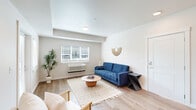 This thoughtfully laid-out 2-bedroom, 1-bathroom residence offers a clean, modern aesthetic across a single floor. The open-concept living room greets you with light hardwood flooring, neutral walls, and large windows that invite abundant natural light. A glass-paneled entry door enhances the airy feel of the space. The kitchen is outfitted with dark wood cabinetry, stainless steel appliances including a refrigerator, range, and over-the-range microwave, and a white breakfast bar with barstool seating — ideal for casual dining. A compact dining area adjacent to the kitchen provides additional mealtime flexibility. Both bedrooms feature plush wall-to-wall carpeting, natural light from exterior-facing windows, and sliding closet doors offering practical storage. A wall-mounted climate control unit is present in the primary bedroom. The shared full bathroom includes a tub-shower combination, tile flooring, and a wood-accented vanity with clean, neutral finishes. Throughout the residence, the consistent use of light tones, recessed lighting, and hardwood-style flooring in common areas creates a cohesive and inviting atmosphere suited for everyday living.