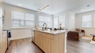 This single-floor residence showcases a clean, modern design characterized by bright white walls, wood-look flooring, and an open layout that promotes a sense of spaciousness and connectivity between living areas. The kitchen serves as a central focal point, featuring a large island with granite countertops, an integrated sink, and bar seating. Light wood cabinetry extends to the ceiling, complemented by stainless steel appliances including a refrigerator, range, and microwave. A sleek linear pendant light anchors the island, while multiple windows fitted with white horizontal blinds allow ample natural light to fill the space. The kitchen flows seamlessly into the living area, which benefits from the same natural light and hardwood-style flooring.

The bedrooms are carpeted and well-proportioned, each featuring windows that bring in natural light. The two bathrooms maintain the space's modern aesthetic, outfitted with granite-topped vanities, wood-toned cabinetry, large mirrors, and wood-look tile flooring. One bathroom includes a shower-tub combination, while the other features a walk-in shower. Throughout the residence, consistent use of natural materials and a neutral color palette creates a cohesive, contemporary ambiance.