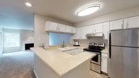 This single-floor residence offers a thoughtfully designed layout that balances comfort and functionality throughout its key living areas. The kitchen is a standout feature, outfitted with crisp white shaker-style cabinetry, light stone-look countertops, stainless steel appliances including an electric range and refrigerator, and a peninsula that provides additional prep space and separates the kitchen from the adjoining living areas. Flush overhead lighting brightens the space effectively. The living room is a welcoming retreat, centered around a classic white-mantled fireplace flanked by windows that invite natural light and offer views of surrounding greenery. Plush wall-to-wall carpeting runs throughout the living and bedroom areas, contributing to a warm, comfortable atmosphere. The bedrooms are generously proportioned, featuring neutral toned walls, carpeted floors, baseboard heating, and windows with outdoor views. One bedroom includes a walk-in closet for added storage convenience. The bathroom is clean and functional, featuring a wide vanity with white cabinetry, a light stone countertop, a large mirror, wood-look vinyl flooring, and a glass-door walk-in shower. The overall aesthetic is light, neutral, and move-in ready.