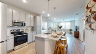 This single-floor residence is designed with a clean, contemporary aesthetic that prioritizes open living and functional flow. The kitchen serves as a central hub, featuring granite countertops, gray cabinetry, stainless steel appliances, a subway tile backsplash, and a large island with an undermount sink and bar seating. Pendant lighting overhead and light wood-style flooring enhance the bright, welcoming atmosphere. The kitchen opens seamlessly into the living area, which is distinguished by a striped sage green accent wall, light hardwood-style flooring, and large windows dressed with sheer curtains that invite generous natural light and outdoor views.

The primary bedroom offers plush carpeting, a ceiling fan, and well-sized windows, with an en-suite bathroom that includes granite vanity counters, gray cabinetry, wood-style flooring, and access to a walk-in closet. A second bedroom is similarly carpeted and well-lit with outdoor-facing windows, accompanied by its own bathroom featuring consistent granite and gray cabinetry finishes. Throughout the residence, neutral tones, recessed lighting, and cohesive material choices create a calm, modern ambiance.