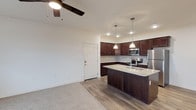 The BLVD At Hays offers a thoughtfully designed single-floor layout that seamlessly blends comfort and modern style. The open-concept living and kitchen area serves as the heart of the space, creating an inviting and functional environment. The kitchen is a standout feature, showcasing rich dark cabinetry that provides generous storage, complemented by sleek granite countertops and a peninsula island with an undermount sink — ideal for both meal preparation and casual dining. Pendant lighting hangs above the island, adding a warm, contemporary touch, while recessed lighting throughout ensures the space is well-lit. Stainless steel appliances, including a refrigerator, microwave, and range, complete the modern kitchen aesthetic. The living area flows naturally from the kitchen, featuring durable wood-style flooring that transitions into plush carpeting, offering a comfortable and versatile space. A ceiling fan anchors the room, providing both functionality and a finishing design detail. Clean white walls and crisp trim maintain a bright, neutral palette throughout, making the space feel open and move-in ready. The unit's single-floor design ensures easy accessibility and a cohesive flow from one area to the next.