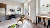Located at 360 Acoma Street in Denver, Colorado, this thoughtfully designed one-bedroom, one-bathroom residence offers a smart and efficient layout across a single floor. The open-concept living and kitchen area greets you upon entry with warm wood-look flooring, soaring ceilings, and generous natural light streaming through large windows flanking a full-light entry door. The kitchen is well-appointed with stainless steel appliances, a gas range, subway tile backsplash, and a two-tone cabinet design featuring white uppers and gray lowers with open shelving for a contemporary touch. The living area provides a flexible space with room for seating and a dining area near the front windows. The bedroom offers a cozy retreat with plush carpet, a bold geometric accent wall, and a sliding-door closet that also houses an in-unit washer and dryer. The bathroom is finished with wood-look tile flooring, a glass-enclosed walk-in shower with white tile surround, a dark-toned vanity, and open ladder shelving for storage. A hallway connects the private and shared areas of the home. The overall aesthetic is modern and clean, making efficient use of every square foot in a stylish, livable manner.