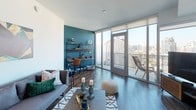 This single-floor residence at 330 13th Street in San Diego presents a contemporary urban design with an open, light-filled layout. The living area is a standout feature, with expansive floor-to-ceiling windows and glass sliding doors that flood the space with natural light and frame sweeping city views. Dark hardwood flooring runs throughout the main living areas, complementing the modern aesthetic. A private balcony accessible from the living room provides an outdoor retreat with open views of the San Diego skyline.

The kitchen is well-appointed with warm wood cabinetry, open shelving, stainless steel appliances including a gas range, built-in microwave, and refrigerator, as well as a sleek tile backsplash and integrated countertops. The design balances functionality with style.

The bedroom offers a quieter retreat, featuring plush carpeting, clean white walls with a subtle gray accent, and a pendant light fixture overhead, creating a calm and restful atmosphere.

The bathroom maintains the clean, minimalist theme with white quartz countertops, an undermount sink, a floating vanity with ample drawer storage, large-format tile flooring, and a backlit mirror, contributing to a crisp, refined finish throughout.