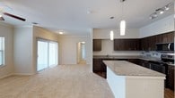 This single-story residence is designed with an open-concept layout that seamlessly connects the kitchen and living areas, creating a cohesive and functional living space. The kitchen is a standout feature, equipped with stainless steel appliances including a range, microwave, dishwasher, and refrigerator with an ice dispenser. Rich, dark espresso-toned cabinetry extends to the ceiling, providing ample storage, while granite-style countertops offer generous prep space. A large kitchen island with a light-toned surface serves as a natural gathering point, illuminated by stylish cylindrical pendant lights. A tile backsplash adds a subtle decorative touch, and track lighting enhances the workspace.

The adjoining living area is carpeted in a neutral, plush tone and receives natural light through a wide sliding glass door fitted with vertical blinds, which opens to the exterior. A ceiling fan overhead adds comfort and airflow. Crown molding and arched interior doorways contribute architectural character throughout the space.

The bathroom features a dual-sink vanity with matching granite-style countertops, dark cabinetry, a large wall mirror, a shower-tub combination, and a well-lit vanity fixture, delivering a clean and functional design.