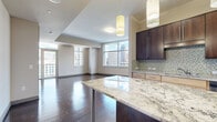 This 2-bedroom, 2-bathroom residence offers a refined urban living experience highlighted by striking city skyline views and upscale finishes throughout. The open-concept kitchen and living area serves as the heart of the home, featuring rich dark hardwood flooring, a large granite-topped center island with pendant lighting, dark wood cabinetry with glass accents, a mosaic tile backsplash, and stainless steel appliances. The living area extends generously from the kitchen, bathed in natural light from floor-to-ceiling windows that frame panoramic city views. Both bedrooms are carpeted and well-proportioned, each benefiting from large windows showcasing the urban skyline and ceiling fans for added comfort. The primary bedroom offers a spacious walk-in closet with extensive wire shelving and organizational systems. The bathrooms are finished with granite-topped dark wood vanities, tile flooring, and tiled soaking tub and shower combinations. A dedicated laundry room houses a full-sized washer and dryer with overhead shelving. The hallway connects all spaces efficiently, with panel-style doors lending a clean, modern aesthetic. This residence combines contemporary design with practical amenities for comfortable city living.