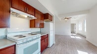 Located at 420 N Third St in Wausau, Wisconsin, this single-floor unit offers a clean, functional layout with an open and airy feel throughout. The kitchen is a standout feature, showcasing rich, warm-toned cabinetry that extends to the upper walls, providing generous storage space. White appliances, including a coil-top electric range and a full-size refrigerator, complement the light gray countertops, while an exhaust hood above the stove adds practicality. The kitchen flows seamlessly into the open living area, which is bathed in natural light from nearby windows. Light wood-style vinyl flooring runs consistently throughout the space, giving it a cohesive and modern appearance. A ceiling fan with a light fixture is centrally positioned in the main living area, enhancing both comfort and brightness. The layout, as visible in the dollhouse view, follows a long, efficient floor plan with distinct zones for living, sleeping, and bathing. The bedroom features a closet with adjustable shelving and curtain panels. The bathroom is finished with wood-style flooring, a toilet, and a tub and sink combination. Baseboard heating is present throughout, ensuring year-round comfort in the Wisconsin climate. Overall, the unit presents a straightforward and well-maintained living environment.