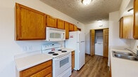Located at 5001 Coopers Landing Dr in Kalamazoo, Michigan, this spacious 5-bedroom, 2-bathroom unit offers a well-organized single-floor layout designed for comfortable living. The kitchen is outfitted with warm oak cabinetry providing ample storage, white appliances including a coil-burner range, over-the-range microwave, and full-size refrigerator, plus clean white countertops and wood-look flooring. A dedicated laundry area with a stacked washer and dryer is conveniently accessible from the kitchen. The five bedrooms are carpeted and feature textured ceilings, neutral walls, and easy access to the hallways. The generously sized primary bedroom offers notable square footage for comfortable furnishing. Closet space is provided within the bedrooms, with at least one featuring a built-in shelving system. The two bathrooms are finished with wood-look flooring and oak vanities — one with a full tub/shower combo and one with a walk-in shower stall. Hallways connect the rooms efficiently, and a staircase is present within the unit. Throughout the space, consistent finishes including textured ceilings, light-toned carpet, and warm wood-trimmed doors create a cohesive and functional living environment.
