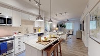 This single-floor residence is thoughtfully designed with an open-concept layout that seamlessly connects the kitchen, dining, and living areas. The kitchen is a standout feature, outfitted with white shaker-style cabinetry, light granite countertops, a neutral tile backsplash, and a full suite of stainless steel appliances. A central island with seating for two is illuminated by a pair of brushed nickel pendant lights, while track lighting runs throughout the shared living spaces. Light wood-look flooring extends across the kitchen and main living areas, contributing to the bright, airy atmosphere.

The living room offers a comfortable, open feel with a ceiling fan, track lighting, and direct sightlines to the dining area. The primary bedroom features plush carpeting, a ceiling fan, and a generous sliding glass door that opens to a private outdoor patio with views of lush greenery. A walk-in closet provides ample storage, and the en-suite bathroom includes a wide white vanity with granite countertops, a large mirror, and a glass-enclosed walk-in shower with tile surround. A second bathroom features wood-look tile flooring and a glass shower enclosure, completing this well-configured residence.