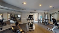 Located at 840 17th St in San Diego's vibrant 92101 zip code, this well-appointed fitness center offers a comprehensive workout environment designed to meet a variety of exercise needs. The space features durable hardwood-style flooring throughout and is finished with neutral gray walls that create a clean, focused atmosphere. Recessed and overhead lighting ensures the room is well-lit at all times.

The facility is equipped with a range of cardio machines, including treadmills, an elliptical trainer, and a rowing machine, alongside a multi-station strength machine, adjustable weight bench, and a dumbbell rack. Full-length wall mirrors are strategically positioned to visually expand the space and allow users to monitor their form during workouts.

Large sliding glass doors and expansive windows along one wall flood the room with natural light and offer direct views of an outdoor courtyard below, which features a life-sized chess set, seating, and lush landscaping — adding a bright and engaging backdrop to any workout. A wall-mounted flat-screen television and a water cooler station add further convenience for users. The room is also served by a central HVAC system with multiple ceiling vents, ensuring year-round climate comfort. A double-door entry provides easy access to and from the rest of the building.