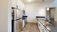 Located at 12310 Moores Lake Rd in Chester, Virginia, this single-floor unit showcases a contemporary design highlighted by an open, airy layout throughout. One of the most striking architectural features is the dramatically tall ceiling in the main living area, where exposed ductwork and expansive floor-to-ceiling windows flood the space with natural light and offer pleasant views of the surrounding greenery. Wood-look flooring in a warm gray tone runs consistently throughout, lending a cohesive and modern aesthetic to every room.

The kitchen is well-equipped with white shaker-style cabinetry fitted with matte black hardware, dark granite countertops, and a full suite of stainless steel appliances including a refrigerator, range, and built-in microwave. Pendant lighting adds a refined touch above the counter space. A set of double doors provides additional storage near the kitchen entry.

The bedrooms are bright and comfortable, with one featuring a ceiling fan and windows overlooking outdoor scenery, while another connects directly to a walk-in closet with built-in shelving. The bathrooms each include a tub-shower combination with clean white tile surround, brushed nickel fixtures, and grab bars, reflecting a thoughtful and accessible design throughout the unit.