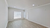 This single-floor space offers a clean, modern aesthetic throughout, with light neutral tones, crown molding, and durable wood-style flooring that flows seamlessly from room to room. The open living area is bright and welcoming, featuring recessed lighting, crisp white trim, and large windows fitted with horizontal blinds that allow generous natural light to fill the space. A glass-panel door provides additional access and connectivity to the outdoors. The kitchen is well-equipped, showcasing gray shaker-style cabinetry, granite-patterned countertops, a double-basin stainless steel sink with a flexible faucet, and a full suite of stainless steel appliances including a refrigerator, range, and over-the-range microwave. The bedroom continues the light, airy feel of the home with a ceiling fan with light fixture, a large window for natural light, and warm wood-tone flooring. The bathroom features dark gray cabinetry with silver hardware, a granite-topped vanity, a large mirror with vanity lighting above, and a clean, functional layout. Throughout the space, thoughtful details such as six-panel doors, consistent flooring, and a neutral color palette create a cohesive and move-in-ready environment.