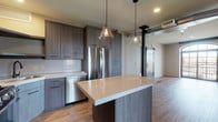 This single-floor space showcases a thoughtfully designed contemporary interior that blends industrial and modern elements throughout. The kitchen serves as a central highlight, featuring grey wood-tone cabinetry extending to the ceiling, a central island with a light quartz countertop, and stainless steel appliances including a gas range, built-in microwave, dishwasher, and refrigerator. Pendant lights with glass cone shades hang above the island, complementing the warm hardwood-style flooring that flows through the main living areas.

A standout architectural detail is the dark wood sliding barn door, which adds a rustic-industrial contrast to the otherwise clean, modern palette. Exposed ductwork in the living area reinforces the industrial aesthetic, while an in-unit stacked washer and dryer offers added convenience.

The bedrooms feature plush carpeting and striking arched windows with black frames that invite abundant natural light and outdoor views. The bathrooms are well-appointed with herringbone tile flooring, white subway and hexagonal tile surrounds, soaking tubs, and matte black fixtures and hardware. One bathroom connects directly to a walk-in closet, enhancing functional flow. Overall, the space presents a cohesive, upscale modern design with carefully curated finishes throughout.
