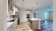 This well-appointed 2-bedroom, 2-bathroom residence in Melbourne, FL offers a thoughtfully designed single-level layout with a clean, contemporary aesthetic throughout. The open-concept living area seamlessly connects the dining room, kitchen, and living room, all finished with wood-look plank flooring that adds warmth and continuity. The gourmet kitchen is a standout feature, showcasing white shaker cabinetry, quartz countertops, a center island with pendant lighting, stainless steel appliances including a French door refrigerator and double wall ovens, a black glass cooktop, and an elegant patterned tile backsplash. Track lighting and a sleek range hood complete the culinary space. The living area benefits from natural light through large windows and provides access to a private balcony. Both bedrooms are carpeted and fitted with ceiling fans; the primary bedroom includes its own well-organized walk-in closet with built-in shelving and hanging systems. The primary bathroom features a dual-sink vanity with white countertops, wood-look tile flooring, and a glass-enclosed walk-in shower with tile surround. Additional highlights include multiple closets, laundry facilities, hallways, and a utility room, offering practical everyday convenience.