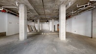 Located at 2323 Dulles Station Blvd in Herndon, Virginia, this single-floor commercial shell space presents a blank canvas for a wide range of business uses. The space is defined by its industrial aesthetic, featuring exposed concrete ceilings, structural concrete columns, and polished concrete floors throughout. Overhead, visible pipework, conduit, and mechanical systems run across the ceiling, offering a raw yet functional framework ready for tenant build-out.

The interior opens into a generously proportioned open floor plan, supported by a grid of concrete columns that define the structural rhythm of the space. Several distinct zones are evident, including open areas well-suited for retail, showroom, or office configurations, as well as utility sections housing mechanical equipment and back-of-house functions.

Natural light enters through large storefront windows and glass entry doors along the street-facing façade, providing clear views of the surrounding Dulles Station development and mature street trees. Additional windows on secondary walls further brighten the interior. The street-level entry with prominent glazing offers strong visibility and accessibility.

The space is currently in shell condition, with subfloor sections exposed in certain areas, indicating readiness for plumbing rough-in. This property presents a versatile opportunity for customization within a well-connected mixed-use corridor.