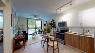Located at 6320 SW Eighth St in West Miami, FL, this thoughtfully designed single-floor residence offers a seamless open-concept layout connecting the kitchen, dining, and living areas. The kitchen is outfitted with stainless steel appliances—including a French door refrigerator, electric range, microwave, and dishwasher—complemented by two-tone cabinetry featuring white upper cabinets and warm walnut-finish lower cabinets, set against light stone countertops. Wood-look tile flooring flows throughout, lending a cohesive and modern aesthetic. The living area is bright and welcoming, benefiting from natural light that pours in through a large sliding glass door opening onto a private balcony with lush tropical views. A ceiling fan and track lighting add both function and style. The bedroom provides a comfortable retreat with a large window, dual reach-in closets, and continued wood-look flooring. The bathroom features a tub-shower combination with wood-look tile surround, a floating walnut vanity with a white countertop, and a large mirror. The unit's entrance is marked by a bold dark front door, setting a contemporary tone from the moment you arrive.