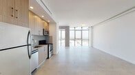Located at 8155 Van Nuys Blvd in Panorama City, California, this contemporary single-floor unit showcases a clean, modern design with an open-concept layout that maximizes both space and natural light. Expansive floor-to-ceiling windows dominate the living area, flooding the interior with sunlight and offering sweeping elevated views of the surrounding Panorama City skyline and neighborhood rooftops.

The polished concrete floors run throughout the main living space, lending an industrial-chic aesthetic that complements the unit's crisp white walls and exposed ceiling details, including a visible conduit pipe that adds an urban loft character. The open living area is generously proportioned, offering flexible arrangement possibilities.

The kitchen is neatly integrated into the living space and features light wood cabinetry with sleek hardware, a stainless steel refrigerator, dishwasher, microwave, and range, along with a single-basin stainless steel sink and neutral countertops. Recessed lighting illuminates the kitchen area effectively.

The bathroom is finished with clean white subway tile surrounding a soaking tub and shower combo, fitted with a glass panel door and chrome fixtures, maintaining the space's modern and minimal aesthetic. A vanity area with warm wood cabinetry provides additional storage and continuity with the kitchen's design palette.
