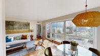This single-floor residence offers a well-considered layout that balances comfort and functionality throughout its thoughtfully arranged rooms. The living area serves as the heart of the home, bathed in natural light streaming through expansive sliding glass doors and large picture windows that frame views of a landscaped outdoor terrace and garden beyond. Parquet flooring flows throughout, lending warmth and a timeless character to the interior. The living space connects seamlessly to a dedicated dining area, distinguished by a corner window and clean, neutral walls.

The kitchen is outfitted with white cabinetry, a gas range, stainless steel refrigerator, and a window above the sink, all set atop grey tile flooring. The two bedrooms are generously proportioned, each featuring parquet floors, soft neutral walls, and ample natural light. One bedroom benefits from corner windows with garden-facing views and room for a seating area. The full bathroom is finished with classic grey tile, a pedestal sink, and a tub-shower combination. Throughout, the space maintains a cohesive, understated aesthetic that feels both livable and refined.