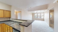 This two-story residence is designed with a practical, open layout that connects the main living areas seamlessly. The kitchen is equipped with light wood cabinetry, dark granite-style countertops, black appliances, and a peninsula with a built-in sink that opens directly to the living area — ideal for everyday functionality. Tile flooring anchors the kitchen, while plush carpet extends throughout the living spaces and bedrooms.

The living area on the main floor features a ceiling fan, neutral warm-toned walls, and a staircase leading to the upper level. Multiple bedrooms are carpeted and include ceiling fans and sliding glass doors that open to private balconies, offering outdoor views and natural light. One upper-level room features clerestory windows along with additional side windows, creating a bright, airy environment.

Bathrooms vary in style: one features a pedestal sink, round mirror, and tile flooring in a compact half-bath configuration, while another includes warm wood vanity cabinetry, a wide white countertop, and a well-lit mirror with a multi-bulb fixture. Throughout, the design maintains a cohesive palette of warm beige tones, white trim, and light flooring.