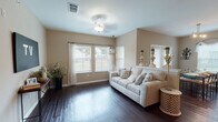 This single-story home offers a cohesive, well-designed layout with warm neutral tones and dark hardwood flooring that flows throughout the main living areas. The entryway welcomes visitors with clean lines and direct access to the rest of the home.

The living room is a standout space, characterized by vaulted ceilings, multiple windows that invite natural light, and a decorative ceiling fan. A hallway framed by a wide archway connects this area to the kitchen and dining room, with stylish pendant lighting guiding the transition.

The kitchen is outfitted with rich dark cabinetry, granite-style countertops, and black appliances including a range, dishwasher, and microwave. Ample upper and lower cabinet storage contributes to its functional design, while the dark hardwood flooring ties it to the adjacent spaces.

The dining area features multiple windows with blinds and valances, providing natural light and a pleasant atmosphere for gatherings. Decorative wall sconces add a touch of elegance.

The bedroom is a comfortable retreat with plush carpeting, a ceiling fan, a window for natural light, and access to a walk-in closet. The bathroom includes dark hardwood flooring, a granite-topped vanity with dark cabinetry, a large mirror, and a shower-tub combination.
