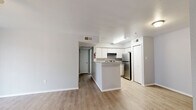 This efficiently laid-out one-bedroom unit offers a thoughtful floor plan that maximizes every square foot across a single level. The open-concept living area is anchored by light wood-style flooring and neutral gray walls, creating a clean, modern aesthetic. A ceiling fan overhead and a large sliding glass door with vertical blinds provide both comfort and natural light, giving the living space an airy, welcoming feel.

The kitchen flows seamlessly from the living and dining areas, featuring white cabinetry, a peninsula with counter seating, stainless steel appliances including a refrigerator and range, and a built-in overhead exhaust. A dedicated pantry offers additional storage convenience. The kitchen's light flooring and bright overhead lighting keep the space feeling open and functional.

The bedroom is carpeted for comfort and benefits from multiple windows that allow generous natural light to filter in. A sliding double-door closet provides practical storage, and the room offers enough space for a comfortable furniture arrangement. Additional closets are distributed throughout the unit, ensuring abundant storage options.

A hallway connects the main living areas to the bedroom and bathroom, maintaining a logical and efficient flow throughout the home. The overall palette of whites, grays, and light wood tones lends the unit a cohesive, move-in-ready appearance.