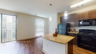 This single-story, one-bedroom, one-bathroom residence showcases a thoughtfully designed open-concept layout that connects the kitchen and living areas seamlessly. The kitchen is a standout feature, equipped with rich dark espresso cabinetry, granite countertops, and a full suite of black appliances including a refrigerator, range, microwave, and dishwasher. A curved peninsula island with matching granite serves as both a functional workspace and an informal dining area, illuminated by stylish pendant lighting overhead. Wood-style flooring runs throughout the main living areas, adding warmth and visual continuity to the space.

The living area is bright and open, benefiting from natural light through large windows with blinds and a sliding glass door that opens to an exterior balcony. The neutral wall tones create a clean, versatile backdrop. In-unit laundry is accessible via a dedicated closet visible from the main corridor, adding everyday convenience. The bathroom features a tiled tub-shower combination, a dark vanity with granite countertop and undermount sink, an overhead storage cabinet, and tile flooring. The consistent use of dark cabinetry and granite finishes throughout gives the unit a cohesive, modern aesthetic.
